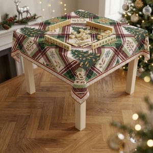 May include: A square table covered with a festive tablecloth featuring a green, red, and white plaid pattern with pine tree and snowflake motifs. A set of wooden mahjong tiles is arranged on the tabletop in a rectangular formation.