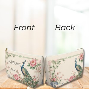 May include: A zippered pouch featuring a cream background with a peacock, pink peony flowers, and bamboo stalks. The front displays the text "MAHJONG" and the name "Sarah" in black script. The back shows a matching peacock and floral design.