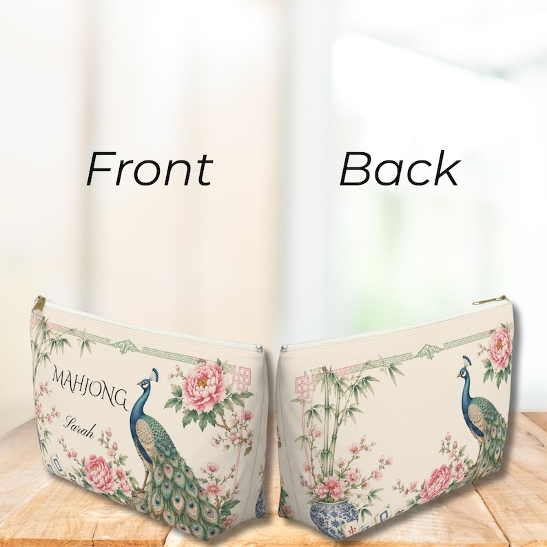 May include: A zippered pouch featuring a cream background with a peacock, pink peony flowers, and bamboo stalks. The front displays the text "MAHJONG" and the name "Sarah" in black script. The back shows a matching peacock and floral design.