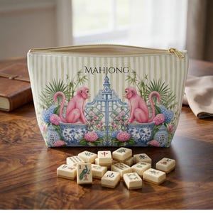 May include: A zippered pouch with a light green and white striped pattern featuring two pink monkeys sitting on blue and white patterned ceramic pots, surrounded by green foliage and pink flowers, with the word MAHJONG printed in black.