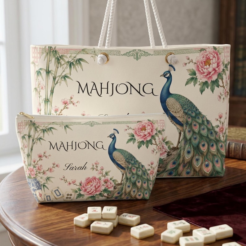 May include: A cream-colored tote bag and a matching zippered pouch, both featuring a printed design of a peacock, pink peonies, and bamboo stalks. The text "MAHJONG" is printed on both items, and the pouch includes the name "Sarah" in script.