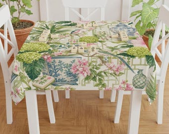 May include: A rectangular tablecloth with a floral and chinoiserie design. The pattern includes pink flowers, blue vases, green foliage, and a lattice background. Mahjong tiles are arranged on the table. The tablecloth is draped over a white table.
