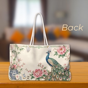 May include: A cream-colored tote bag with white rope handles featuring a printed design of a blue and green peacock, pink peony flowers, bamboo in a blue and white vase, and mahjong tiles. The word Back is printed in the upper right corner.