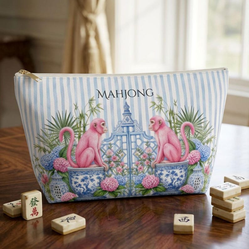 May include: A zippered pouch with a light blue and white vertical striped pattern. The front features two pink monkeys sitting in blue and white patterned pots, flanking a central gate, with floral accents and the word MAHJONG printed above.