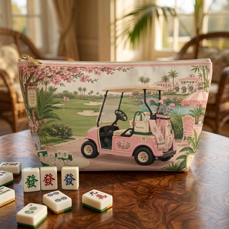 May include: A zippered pouch featuring a printed scene of a pink golf cart on a green course with cherry blossoms, palm trees, and a clubhouse. In the foreground, several white mahjong tiles with green and red characters are scattered on a table.