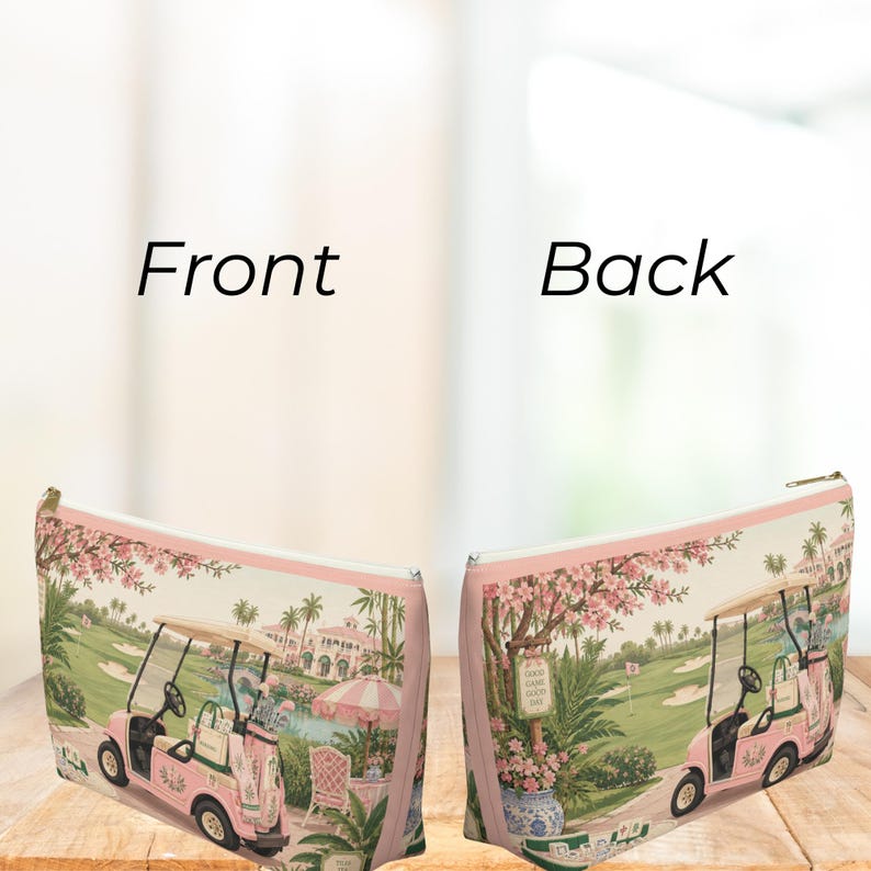 May include: A rectangular zippered pouch featuring a pink golf cart on a golf course with palm trees and a building in the background. The design includes a pink and white striped umbrella, a floral tree, and a sign that reads Good Game Good Day.