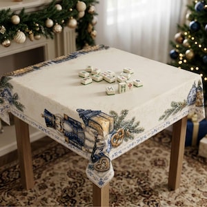 May include: A square tablecloth with a cream background featuring a printed border of blue nutcrackers, pine branches, and pretzels. Several white mahjong tiles with green and red symbols are scattered across the center of the fabric surface.