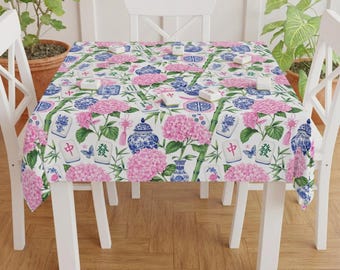 Puede incluir: Un mantel blanco con un patrón repetitivo de racimos de hortensias rosas, tarros de jengibre de porcelana azul y blanca, tallos de bambú verde, pequeñas mariposas azules y fichas de mahjong con caracteres chinos rojos y verdes impresos.
