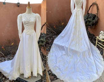 Könnte beinhalten: Ein weißes Vintage-Hochzeitskleid mit langen Ärmeln und einem Spitzenoberteil. Das Kleid hat einen vollen Rock und einen Schleier.