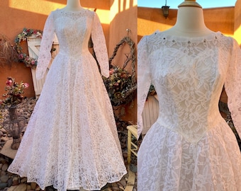 May include: A white lace wedding dress with long sleeves and a fitted bodice. The dress has a full skirt and is adorned with delicate beading around the neckline.