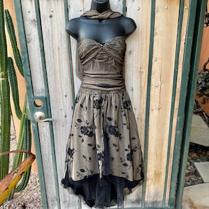 May include: A black and gold strapless dress with a black tulle overlay and floral embroidery. The dress has a sweetheart neckline and a fitted bodice. The skirt is full and flowing.