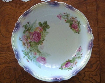May include: A white porcelain bowl with a scalloped edge and a floral design. The bowl has a light blue and purple iridescent glaze. The floral design features pink roses, green leaves, and purple flowers.