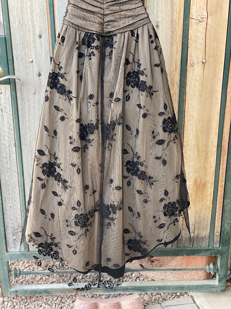 May include: A black tulle skirt with a floral pattern. The skirt is gathered at the waist and has a full, flowing silhouette.