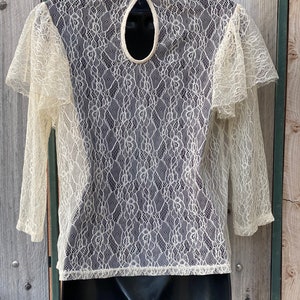 May include: A white lace top with a keyhole back and 3/4 sleeves. The top is sheer and has a delicate floral pattern.