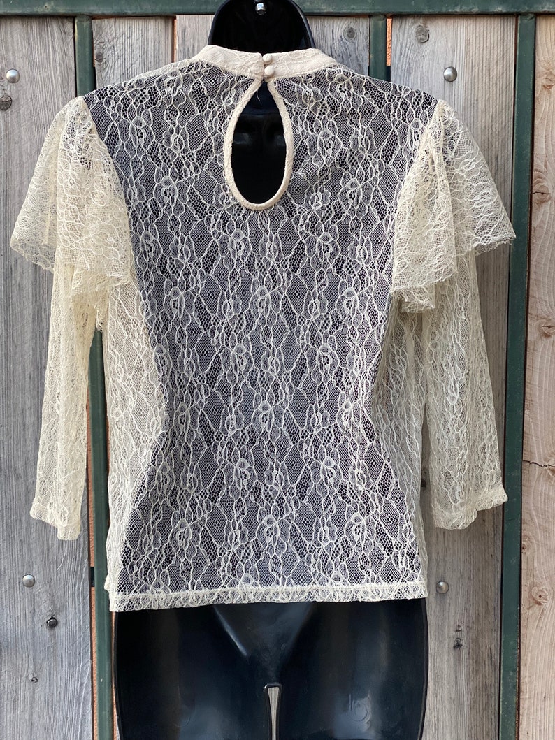 May include: A white lace top with a keyhole back and 3/4 sleeves. The top is sheer and has a delicate floral pattern.