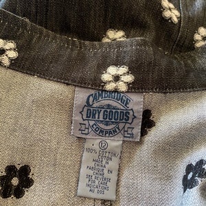 May include: A black and white floral print fabric with a white tag that reads "CAMBRIDGE DRY GOODS COMPANY" and "100% COTTON/COTON MADE IN CHINA FABRIQUE EN CHINE SEE REVERSE FOR CARE INDICATIONS AU DOS" with a size 12 label.