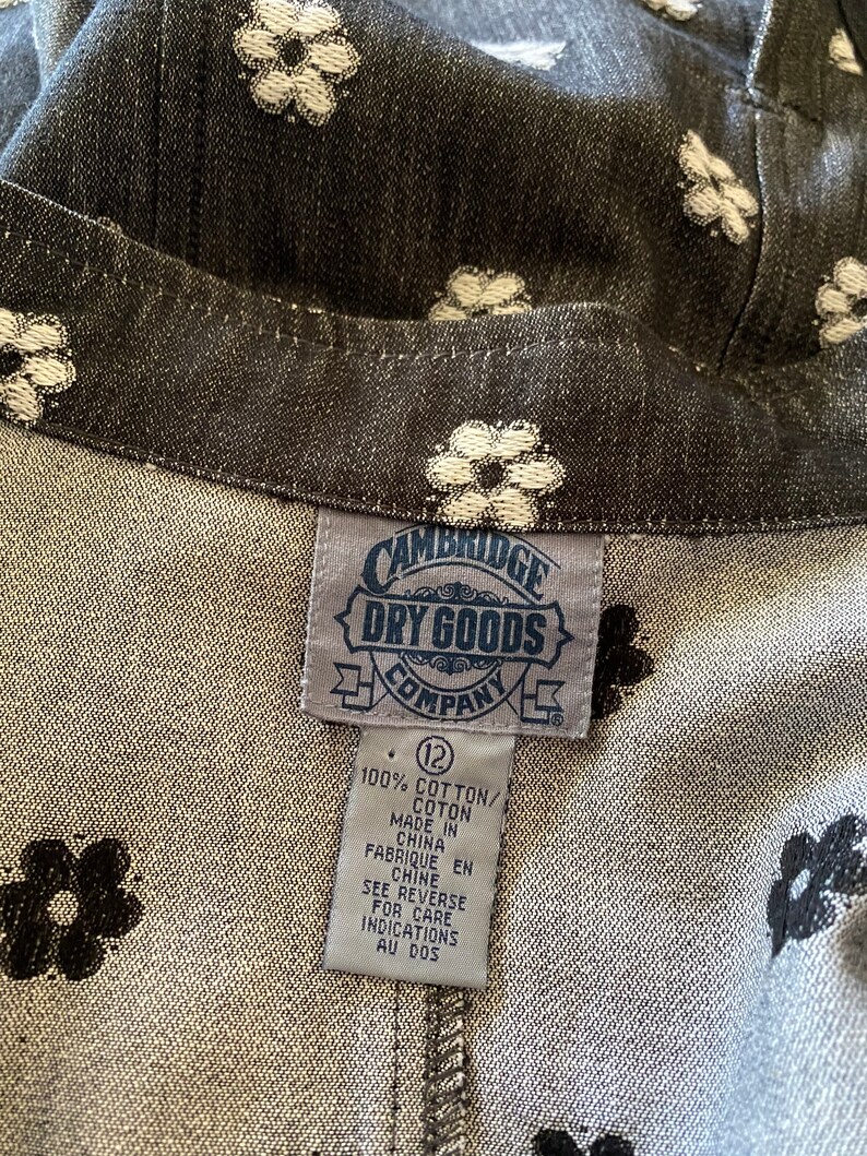 May include: A black and white floral print fabric with a white tag that reads "CAMBRIDGE DRY GOODS COMPANY" and "100% COTTON/COTON MADE IN CHINA FABRIQUE EN CHINE SEE REVERSE FOR CARE INDICATIONS AU DOS" with a size 12 label.