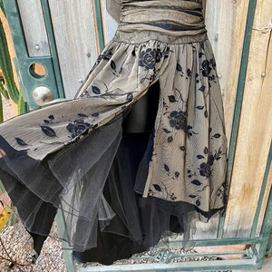 May include: A black and beige tulle dress with a floral pattern. The dress has a fitted bodice and a full skirt. The skirt has a slit in the front and is layered with tulle.
