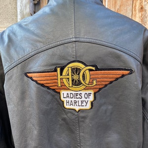 Puede incluir: Chaqueta de cuero negra con un gran parche bordado en la espalda que dice "HOG Ladies of Harley".
