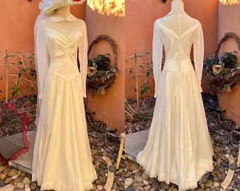 Könnte beinhalten: Ein Vintage-Hochzeitskleid aus weißer Spitze mit langen Ärmeln und einem taillierten Oberteil. Das Kleid hat einen vollen Rock und einen Spitzenbesatz. Das Kleid wird auf einer Puppe mit einem weißen Hut und Schleier gezeigt.