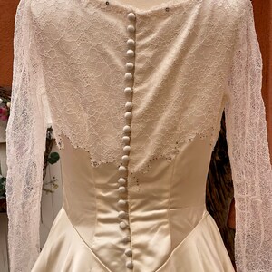 May include: A white satin wedding dress with a lace overlay and a row of buttons down the back.