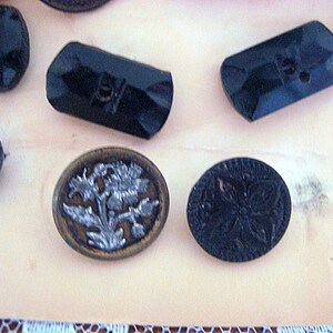 May include: Assortment of black and silver buttons with various designs. Some buttons are round, while others are rectangular. One button features a floral design.