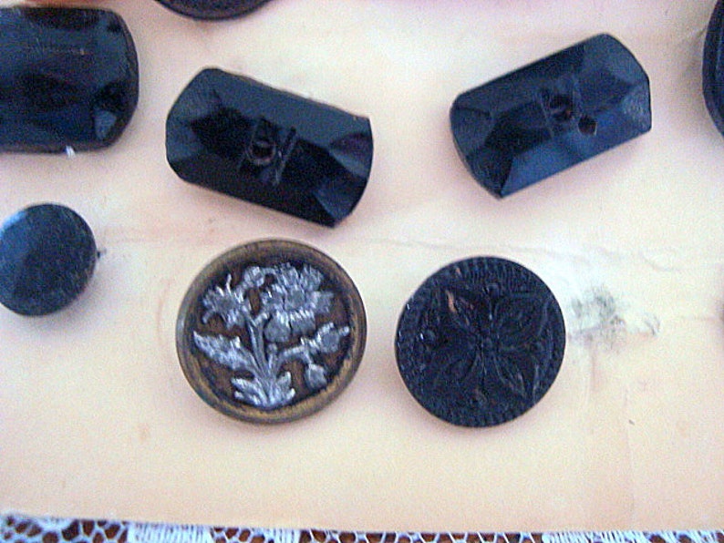 May include: Assortment of black and silver buttons with various designs. Some buttons are round, while others are rectangular. One button features a floral design.