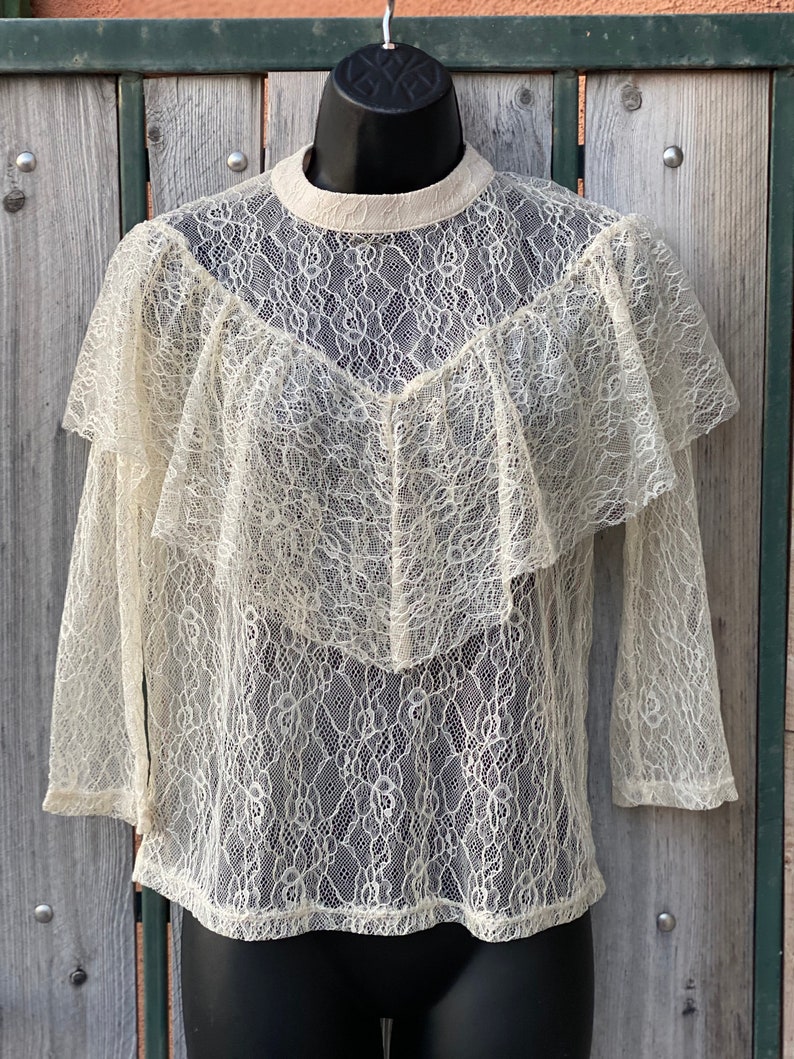 May include: A white lace top with a ruffled neckline and long sleeves.