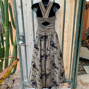 May include: A long, brown and black formal dress with a halter neckline and a floral pattern. The dress has a fitted bodice and a flowing skirt.
