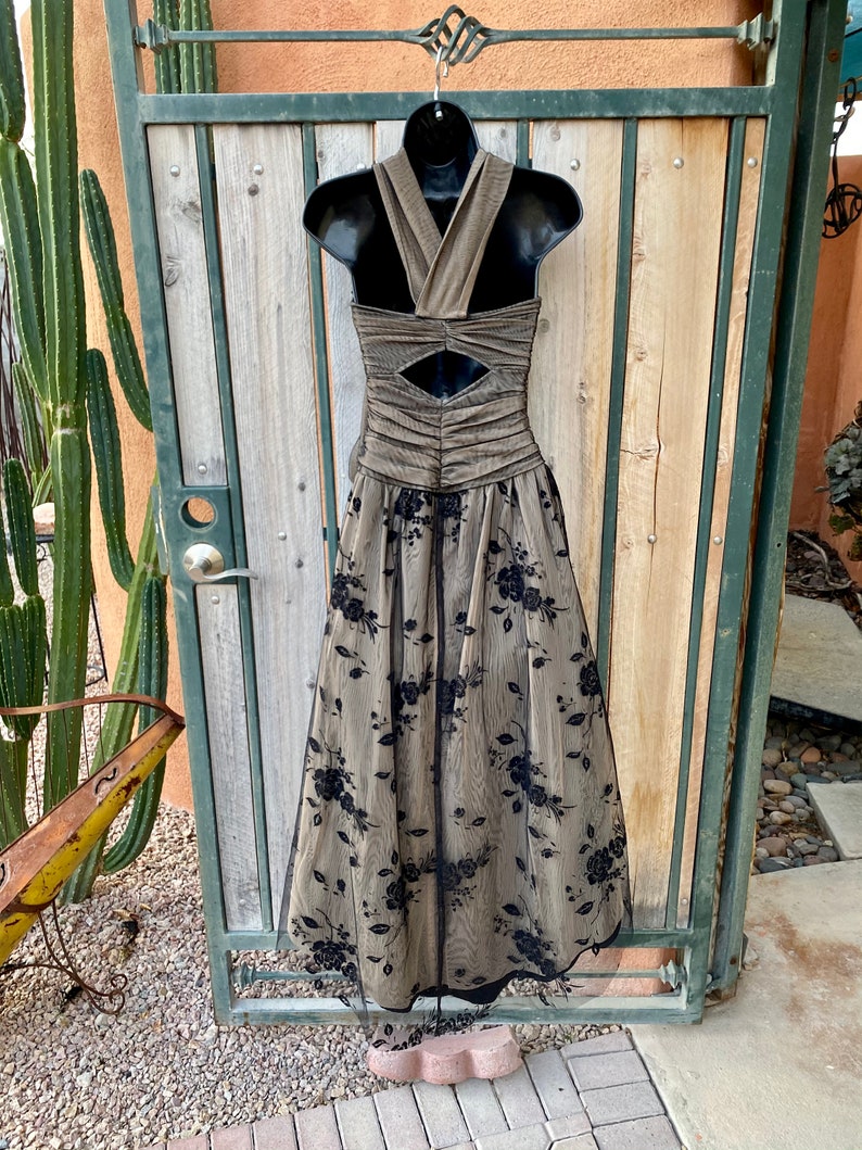 May include: A long, brown and black formal dress with a halter neckline and a floral pattern. The dress has a fitted bodice and a flowing skirt.