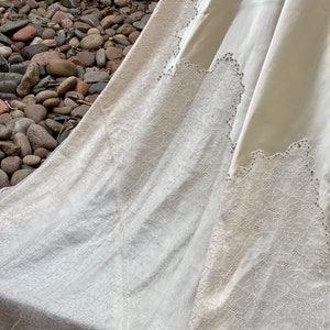 May include: A white wedding dress with a lace trim and beaded accents. The dress is made of a soft, flowing fabric and has a long train.