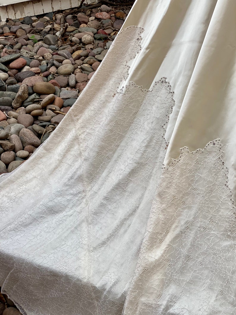 May include: A white wedding dress with a lace trim and beaded accents. The dress is made of a soft, flowing fabric and has a long train.