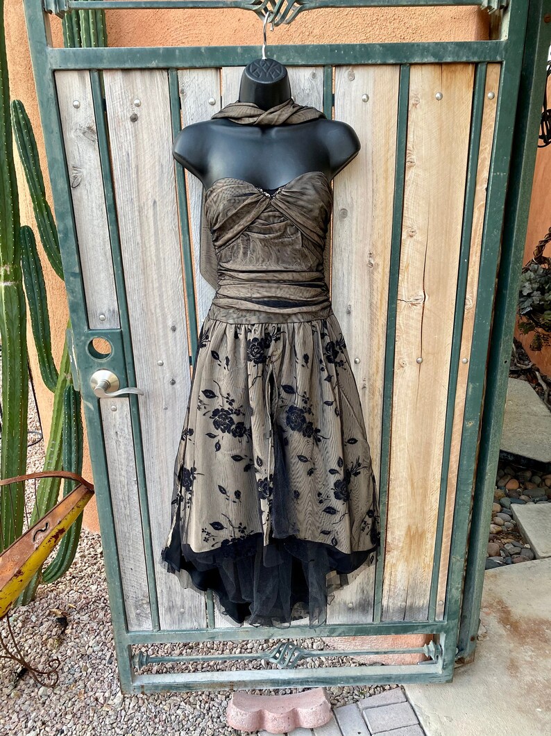 May include: A black and gold strapless dress with a black tulle overlay and floral embroidery. The dress has a sweetheart neckline and a fitted bodice. The skirt is full and flowing.