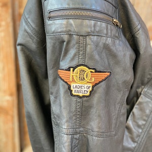 Puede incluir: Chaqueta de cuero negra con un parche bordado en marr&oacute;n y dorado que dice "HOG Ladies of Harley".