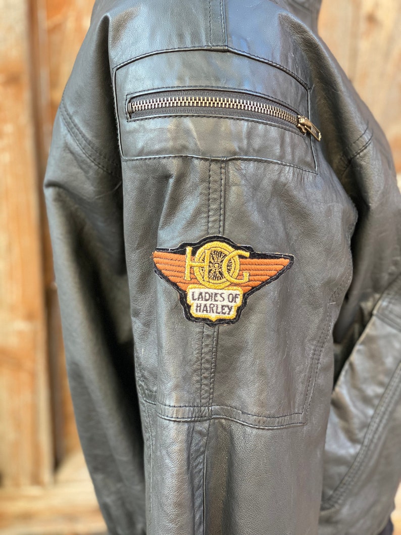 Puede incluir: Chaqueta de cuero negra con un parche bordado en marr&oacute;n y dorado que dice "HOG Ladies of Harley".