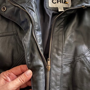 Puede incluir: Chaqueta de cuero negra con cierre de cremallera y una etiqueta que dice "CHIA Hecho en China".