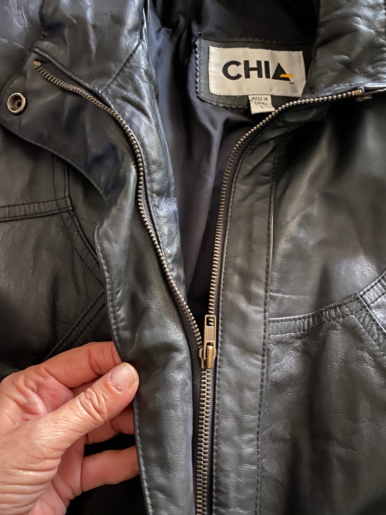 Puede incluir: Chaqueta de cuero negra con cierre de cremallera y una etiqueta que dice "CHIA Hecho en China".