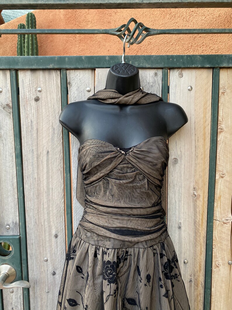 May include: A brown and black strapless dress with a floral pattern. The dress has a fitted bodice and a flowing skirt.