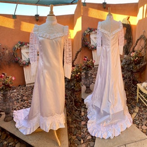 May include: A white satin wedding dress with long lace sleeves and a high neckline. The dress has a fitted bodice and a flowing skirt with a train. The dress is decorated with lace trim and ruffles.