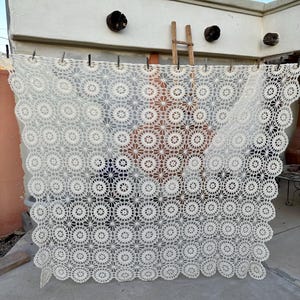 May include: A white crocheted tablecloth with a scalloped edge and a repeating pattern of circles and flowers.