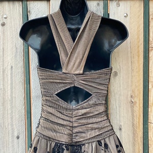May include: A brown and black formal dress with a criss-cross halter neckline and a keyhole cutout in the back. The dress has a tulle skirt with black floral embroidery.