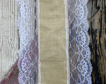 May include: A burlap table runner with white lace trim. The runner is a natural beige color and the lace is a crisp white.