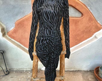 May include: A black long-sleeve dress featuring a high neckline and a dark gray zebra stripe pattern. The garment has structured shoulders and a gathered, draped fabric detail at the waist that creates an asymmetrical hemline.