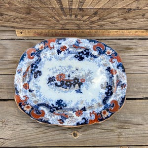 May include: An oval serving platter with a blue and white floral pattern and red accents. The platter has a gold rim and is made of ceramic.