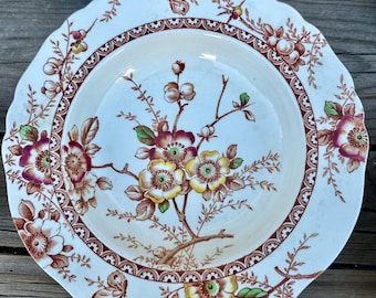 May include: A set of antique ceramic plates with a floral design. The plates have a cream background with brown, yellow, and burgundy floral patterns. The rims have a scalloped edge and a decorative brown border. Suitable for serving food.