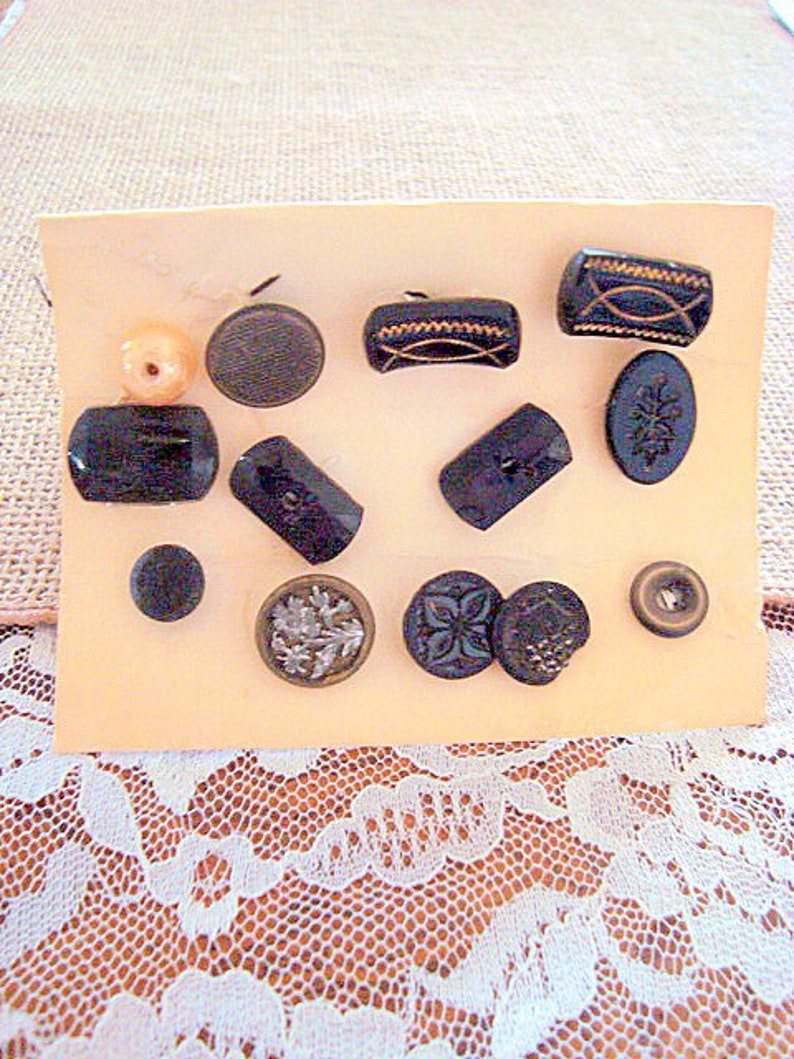 May include: Assortment of black and white buttons with various designs and shapes, including a floral design, a geometric design, and a plain button. The buttons are displayed on a light orange card.