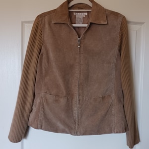 May include: A brown suede jacket with a zipper closure and ribbed knit sleeves. The jacket has a small patch pocket on the front and a label that reads "A.M.I."