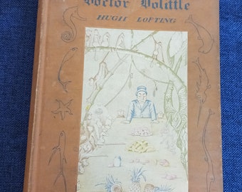 Puede incluir: Un libro marrón con el título "The True Story of Doctor Dolittle" de Hugh Lofting. La portada presenta una ilustración del Doctor Dolittle rodeado de animales en un entorno de selva.
