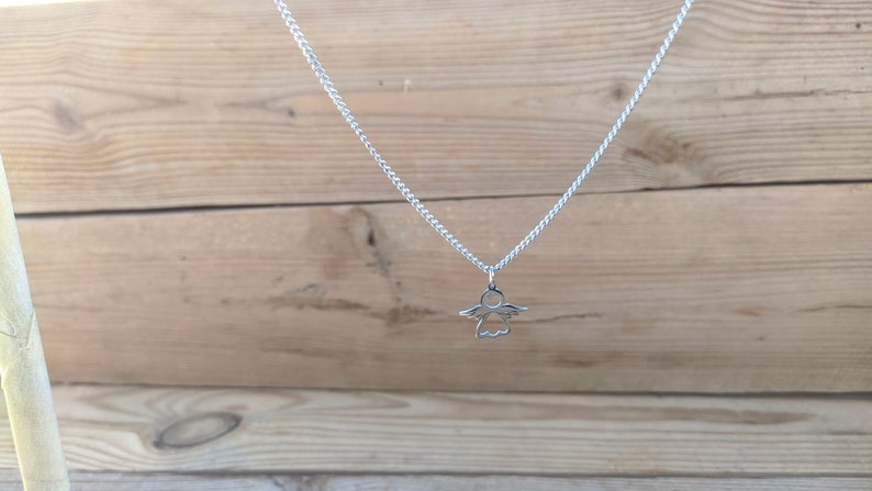 May include: A silver chain necklace with a small angel pendant.