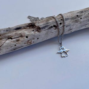 May include: A silver chain necklace with a small angel pendant. The pendant is a cutout design of an angel with wings.
